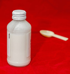 White bottle with medical drug syrup and a small spoon