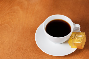 White coffee cup and gold gift box with bow on wooden background