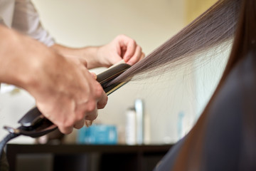 stylist with iron straightening hair at salon