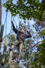 Tuinposter young man  climbing in adventure park, rope park  © wip-studio