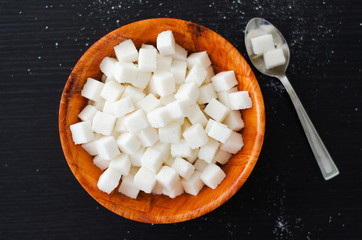 White sugar cubes in wooden bowl with spoon on dark table