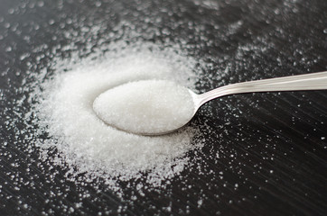 white sugar scattered on a metal spoon black table
