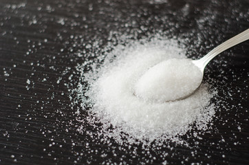 white sugar scattered on a metal spoon black table