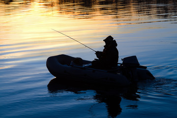 Fishermen on a boat with a fishing rod on the river at sunset