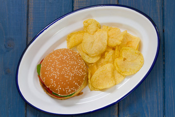 hamburger with potato chips on white dish on blue background