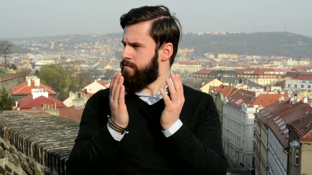 young handsome man with full-beard (hipster) covers his face with arms and then he is suprised - city in background