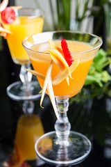 bright glasses with cold alcoholic cocktail with orange juice on a wooden table in a restaurant with creative decoration of berries, fresh mint and orange slices. soft focus