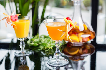 bright glasses with cold alcoholic cocktail with orange juice on a wooden table in a restaurant with creative decoration of berries, fresh mint and orange slices. soft focus