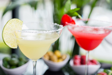 mix of the two bright cocktails: lime daiquiri and strawberry daiquiri on a table with creative decoration of salt on the edge of the glass with fresh mint and lime slices and berries.