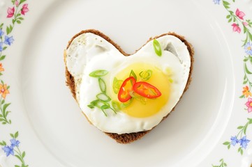 Fried egg heart rye sandwich with scallion and chili on white pl