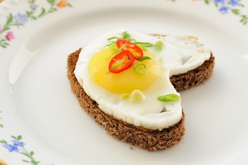 Fried egg heart rye sandwich with scallion and chili on white pl