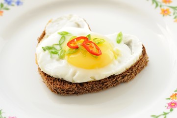 Fried egg heart rye sandwich with scallion and chili on white pl