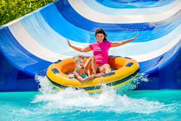 Child with mother on water slide at aquapark. - 83936573