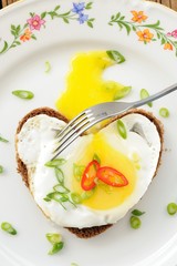 Fried egg heart rye sandwich with scallion, chili and fork on wh