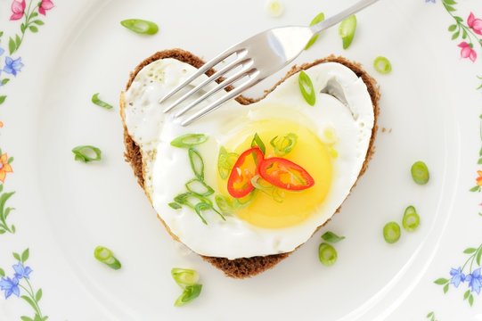 Fried egg heart rye sandwich with scallion, chili and fork on wh