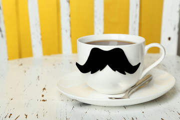 White cup with paper mustache on white wooden background