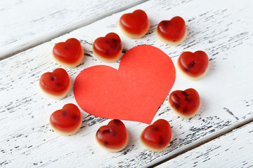 Colorful jelly candies with paper heart on white wooden backgrou