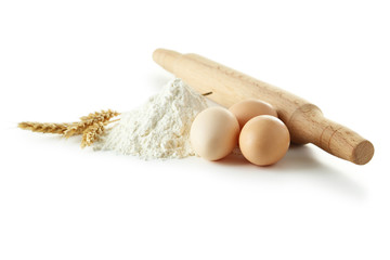 Heap of wheat flour with eggs, rolling pin and spikelets isolate