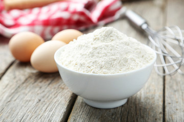 Bowl of wheat flour with eggs and whisk 