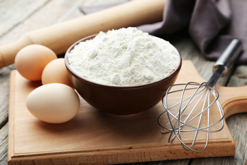Bowl of wheat flour with eggs and whisk on grey wooden backgroun