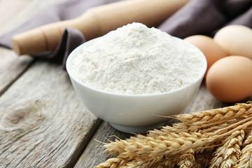 Fototapeta na wymiar Bowl of wheat flour with spikelets on grey wooden background