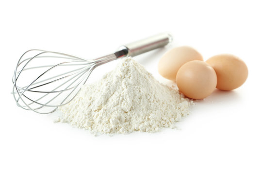 Heap of wheat flour with eggs and whisk isolated on white