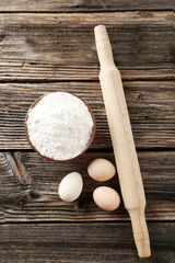 Rolling pin with eggs and bowl of wheat flour 