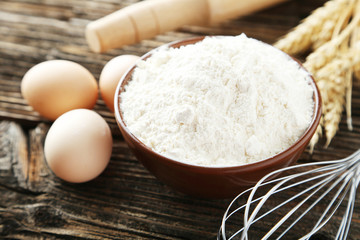 Bowl of wheat flour with eggs and whisk on brown wooden backgrou