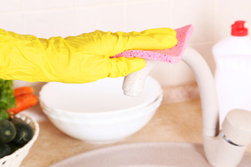 Male hand in gloves with sponge washing faucet