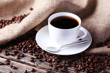 Cup of coffee with coffee beans on brown wooden background