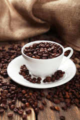 Cup full of coffee beans on brown wooden background