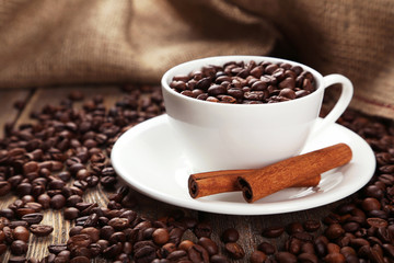 Cup full of coffee beans with cinnamon on  wooden background