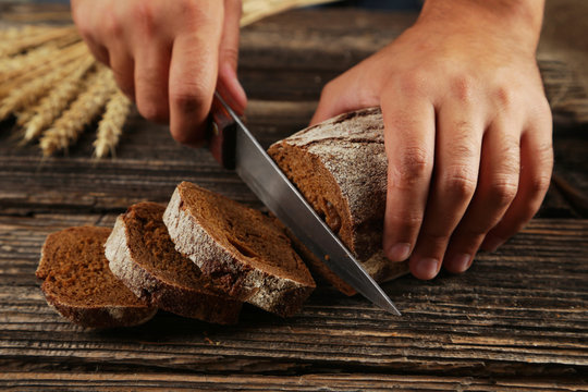 Male hands slicing bread on brown wooden background