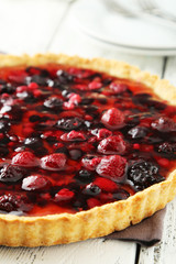 Fresh berry tart on white wooden background