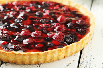 Fresh berry tart on white wooden background