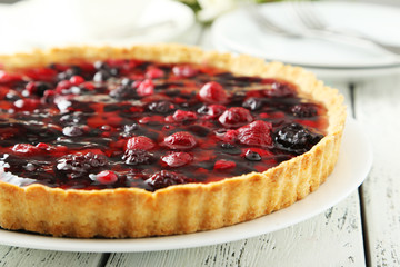 Fresh berry tart on plate on white wooden background