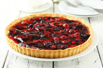 Fresh berry tart on plate on white wooden background