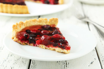 Fresh berry tart on plate on white wooden background
