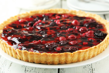 Fresh berry tart on plate on white wooden background