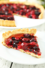 Fresh berry tart on plate on white wooden background