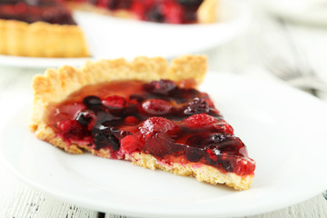 Fresh berry tart on plate on white wooden background