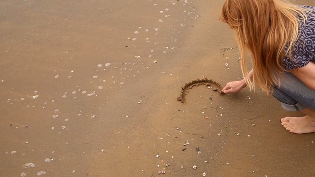 Woman draw heart symbol on sandy beach