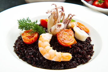 Black rice with sliced squids ,prawns and tomato on white plate