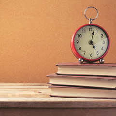 Naklejka premium Alarm clock on stack of books on wooden table
