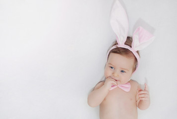 cute little happy baby boy with rabbit's ears lying on soft whit