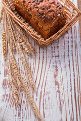 Loaf of bread in wicker basket golden wheat ears on vintage wood