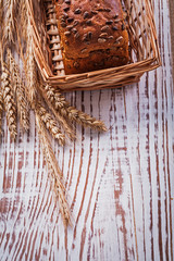 Loaf of bread with seeds in wicker basket wheat ears on vintage 