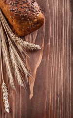 Loaf of brown bread with wheat ears on vintage wooden pine board