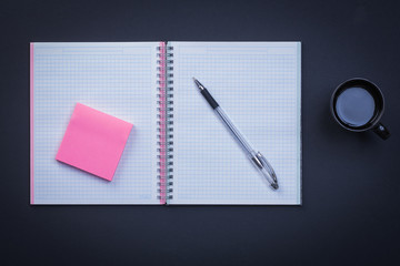 Open notepad pen sticky note and cup of coffee on black backgrou