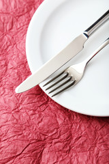 Fork, knife and plate on red background